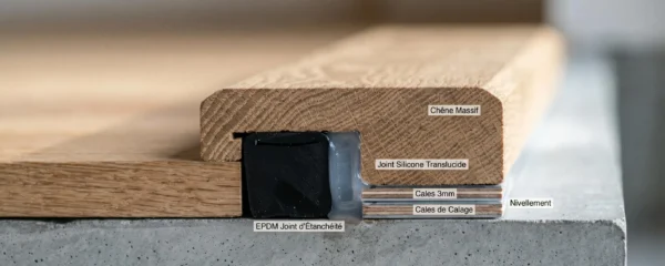 Vue en coupe d'un seuil de porte en chêne révélant les strates d'étanchéité : bande périphérique noire, joint silicone et calage précis, éclairage rasant soulignant les textures bois et matériaux